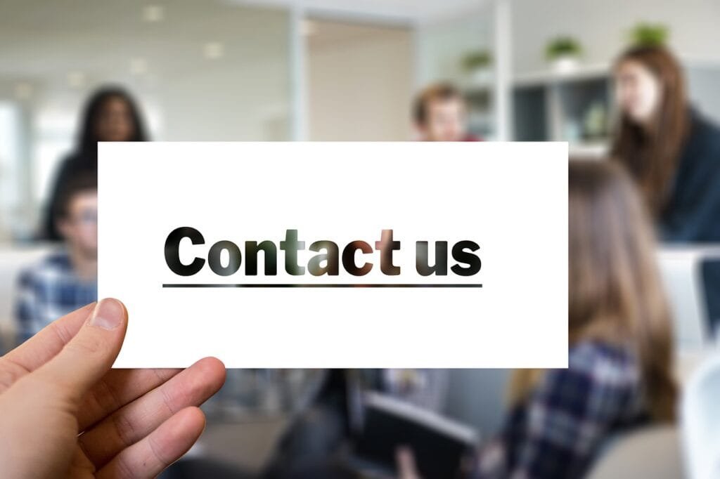 Hand holding a 'Contact us' card in a modern office setting.